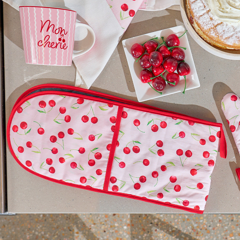 Oven mitt and pot holder with cherry pattern on a kitchen counter with a mug and plate of cherries.