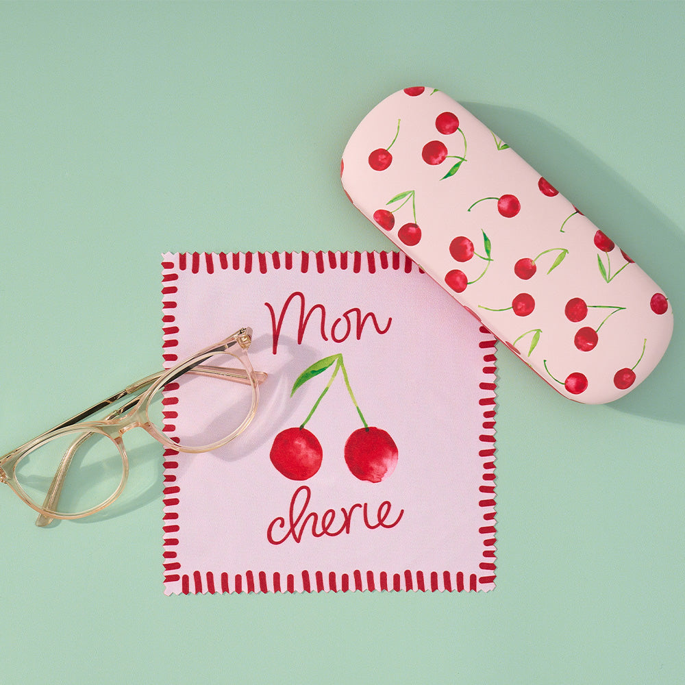 Pink eyeglass case with cherry design and matching pouch on a light green background