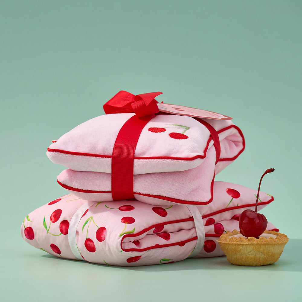 Stack of cherry-patterned heat pillows with a red ribbon on a light green background