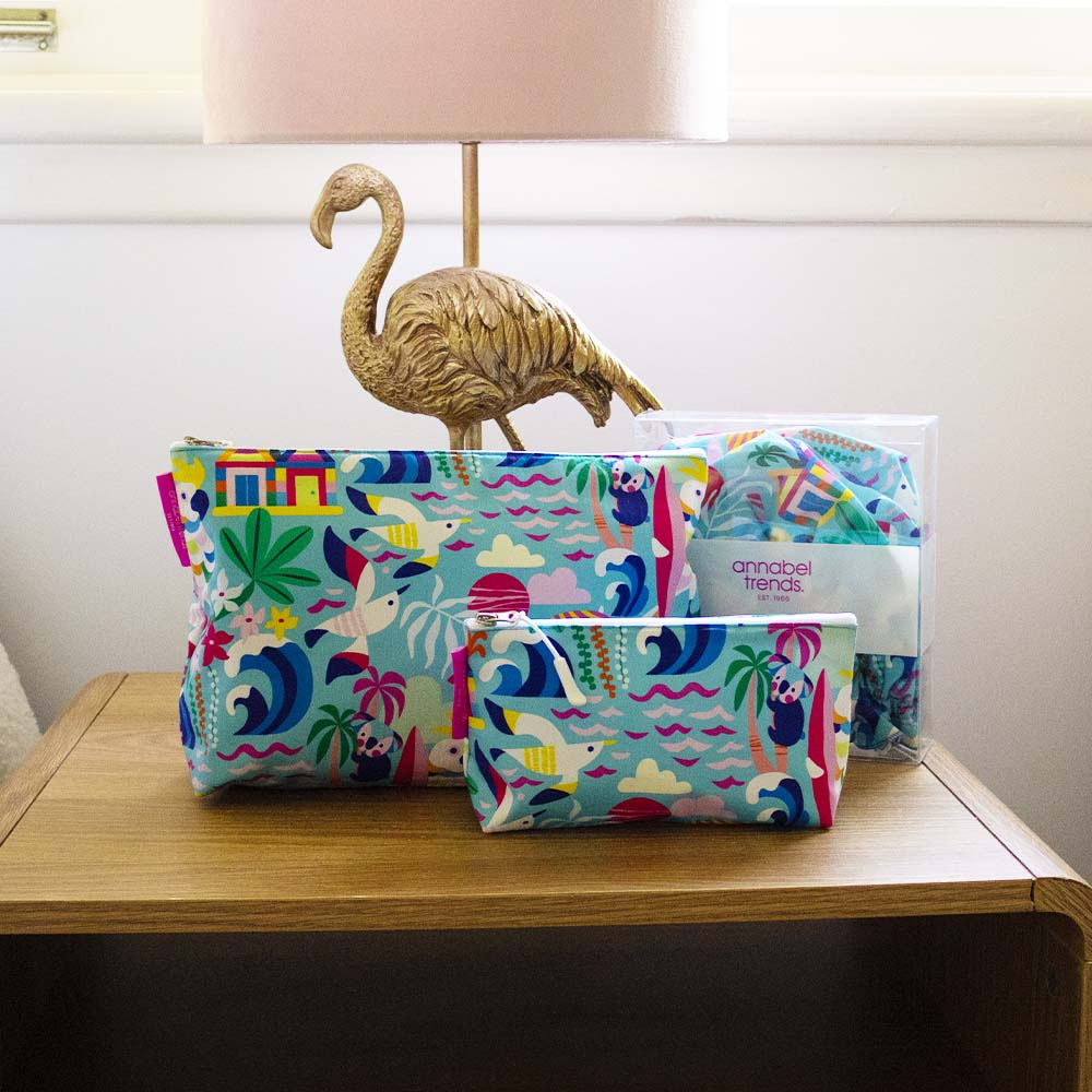 Colorful patterned cosmetuc bags on a wooden surface with a lamp and flamingo decoration in the background.