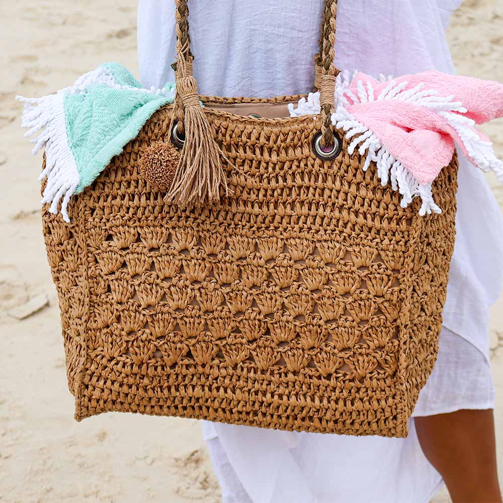 Brown crochet bag with tassels and beach towels on a sandy background