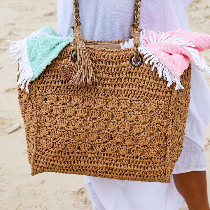 Brown crochet bag with tassels and beach towels on a sandy background