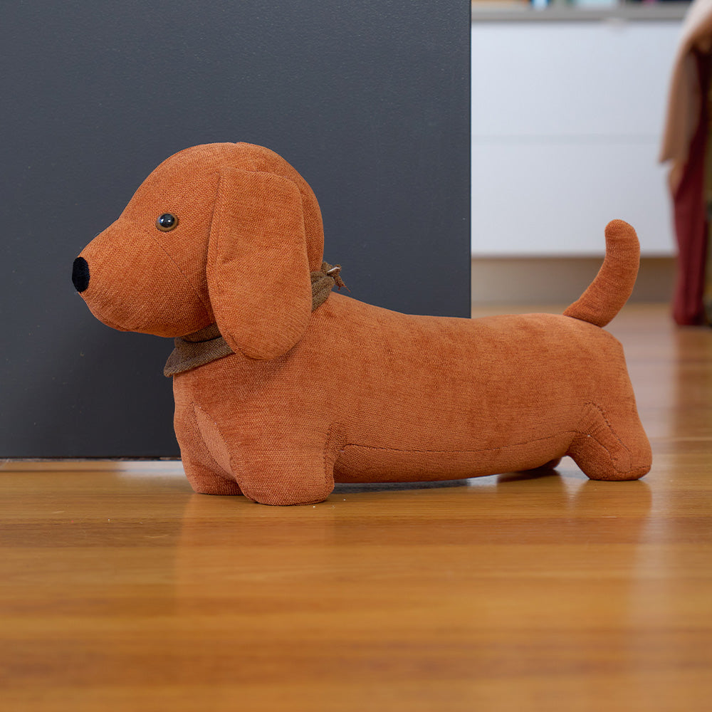 Brown dog-shaped door stopper on a wooden floor with a dark wall in the background