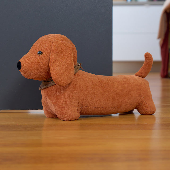 Brown dog-shaped door stopper on a wooden floor with a dark wall in the background