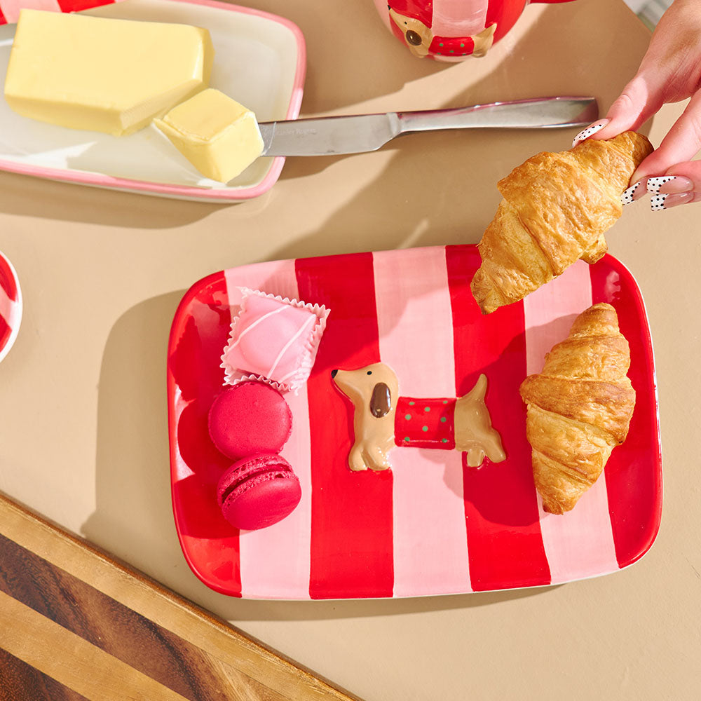 Red and pink striped tray with croissants, macarons, and cookies on a beige surface.