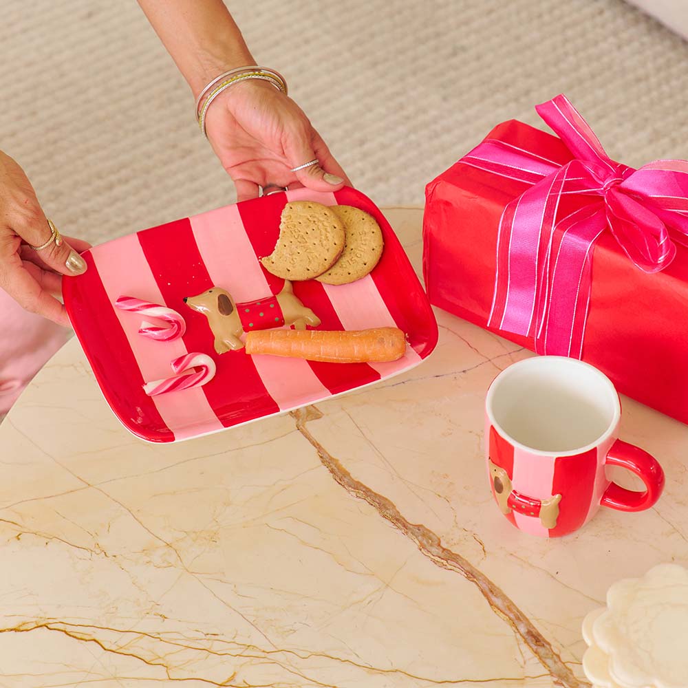 Red and white striped tray with cookies and a carrot, next to a red mug and gift box on a marble surface.