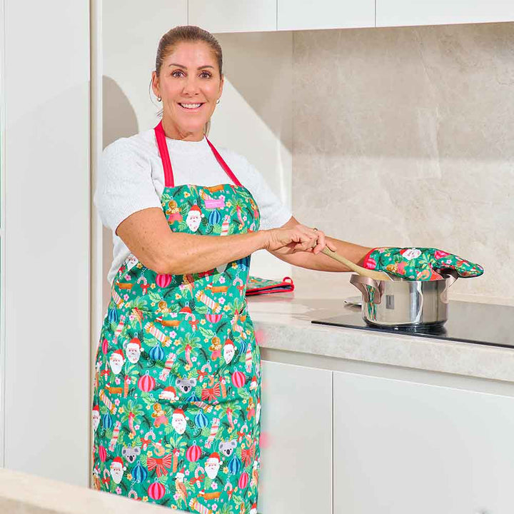 Woman in a kitchen wearing a colorful apron and oven mitts.