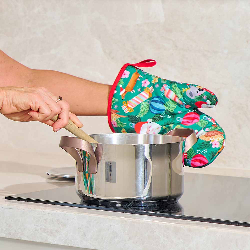 Person wearing a colorful oven mitt while handling a pot on a stove.