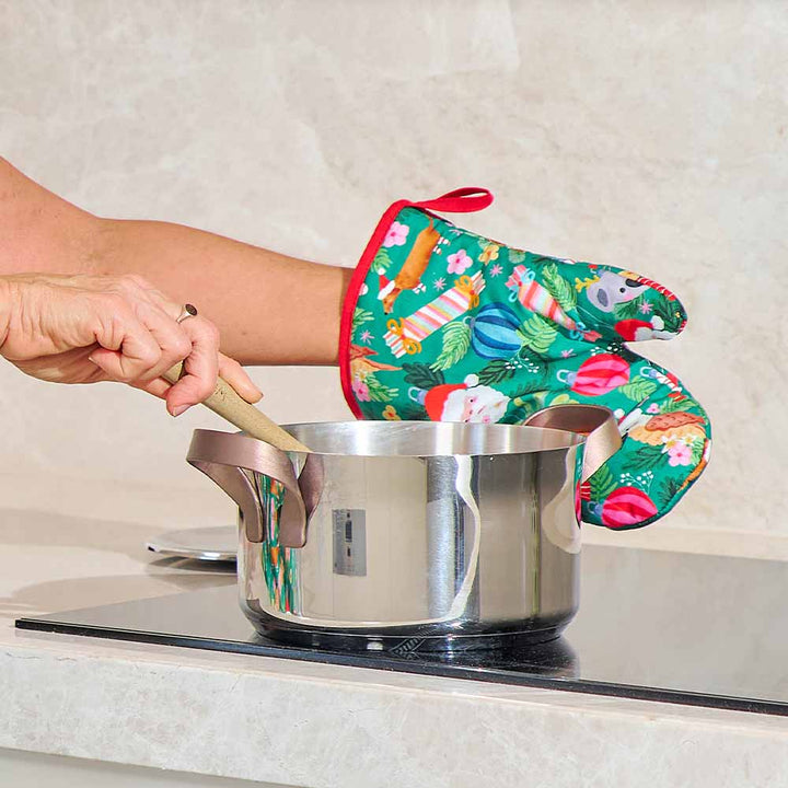 Person wearing a colorful oven mitt while handling a pot on a stove.
