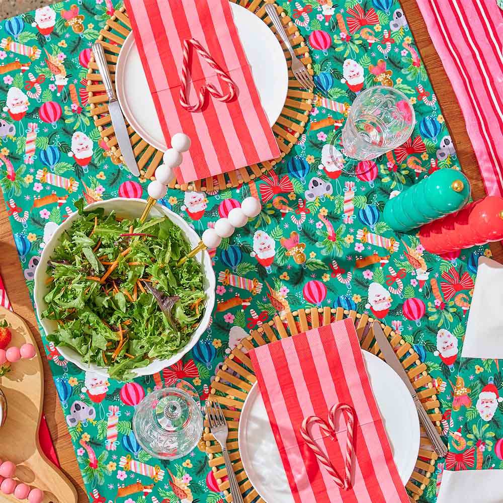 Colorful table setting with Christmas-themed placemats, red and white striped napkins, and a bowl of salad.