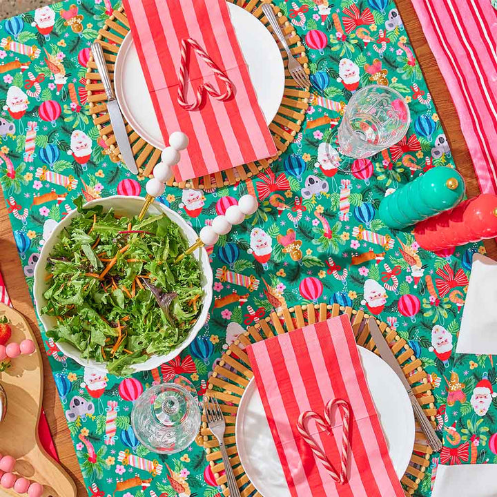 Colorful table setting with Christmas-themed placemats, red and white striped napkins, and a bowl of salad.