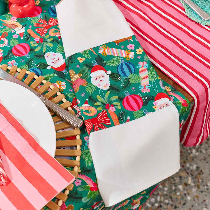 Christmas-themed table setting with green placemats featuring Santa Claus, white plates, and red striped napkins.