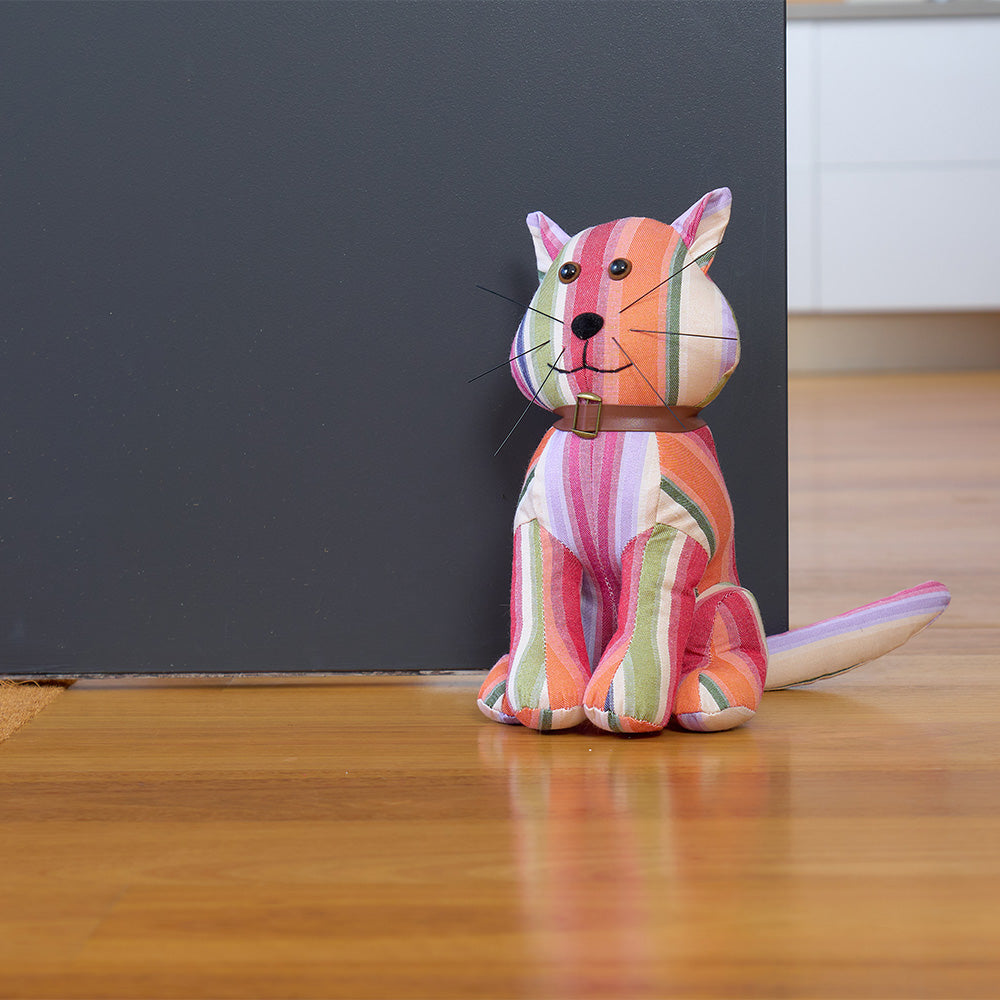 Colorful striped cat-shaped doorstop on a wooden floor with a dark wall background