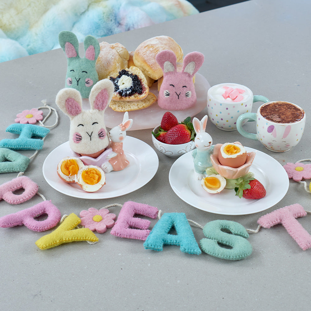 Easter-themed table setting with plush bunnies, eggs, and a 'Happy Easter' banner.