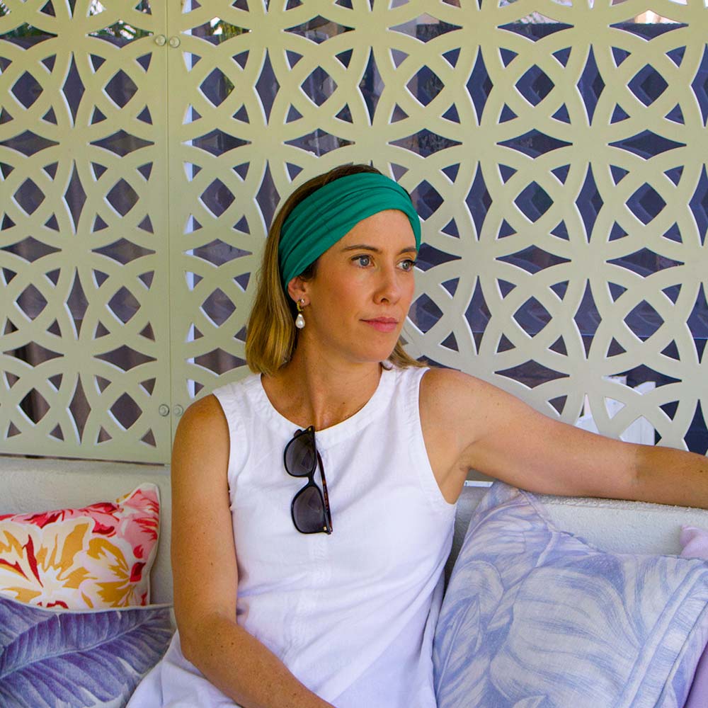 Woman wearing a green headband sitting against a decorative wall with pillows.