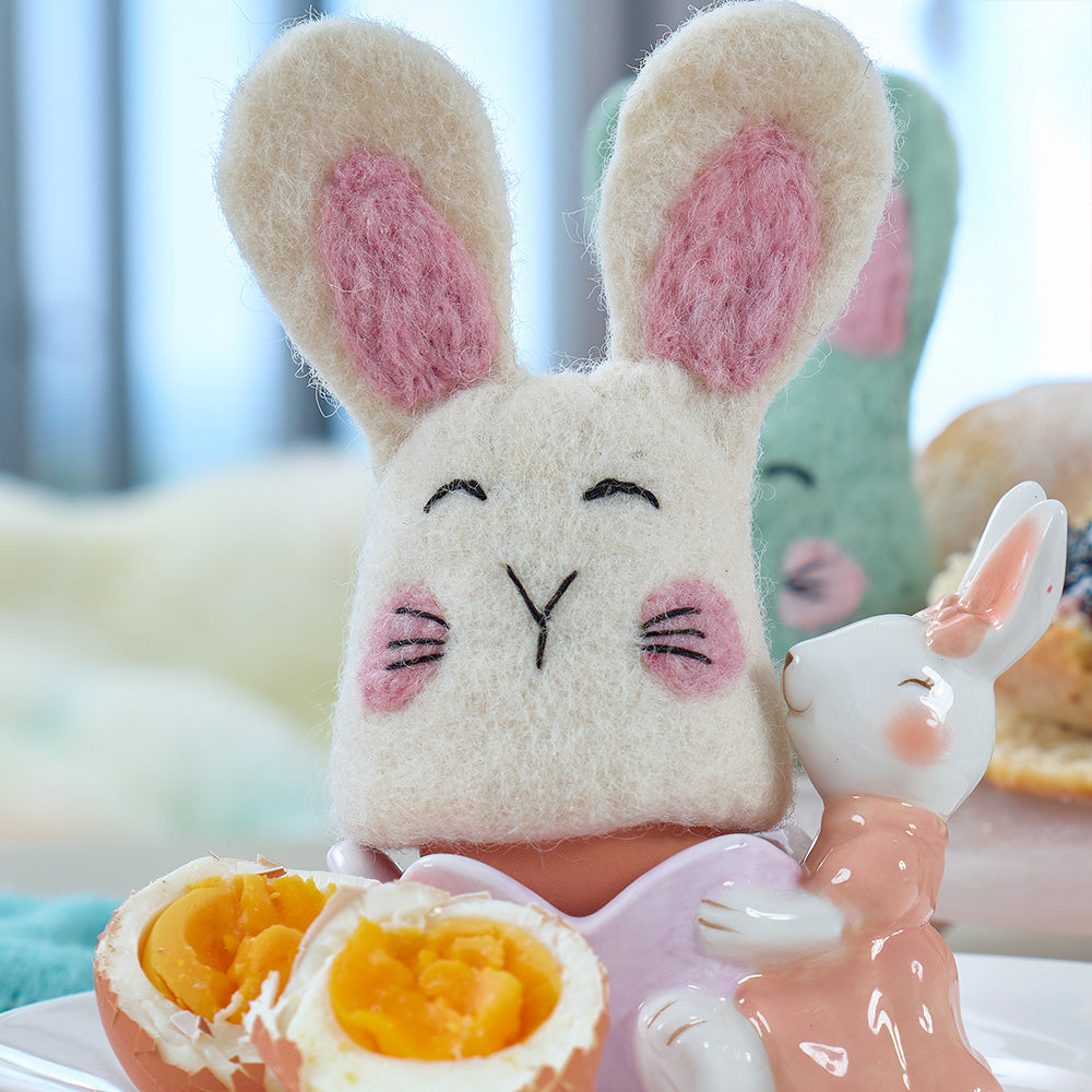 Felted bunny egg warmer with on top of boiled egg in a ceramic egg cup