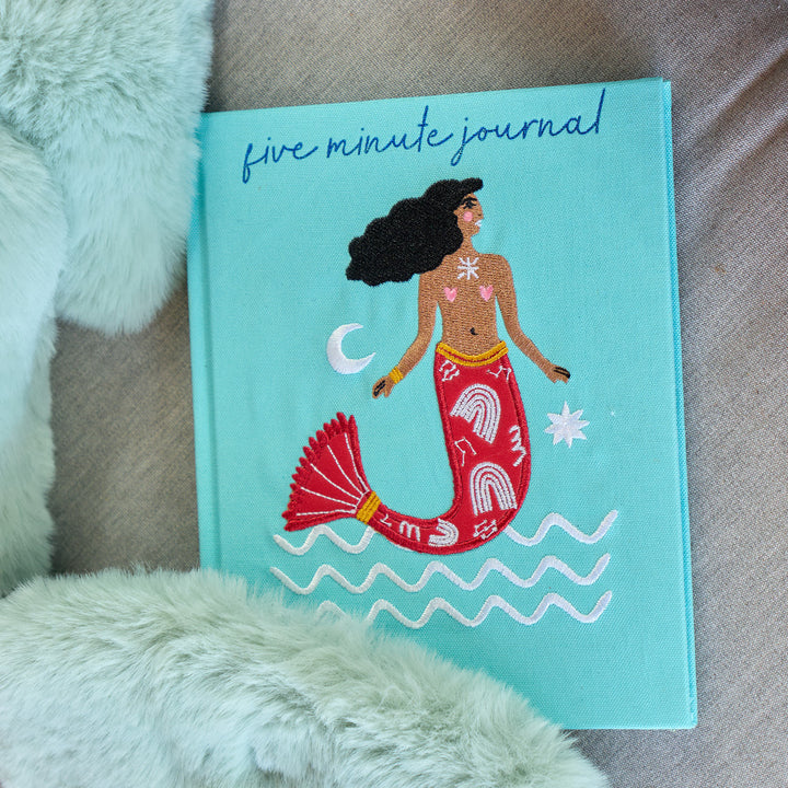 Five minute journal with mermaid embroidered illustration on a textured surface