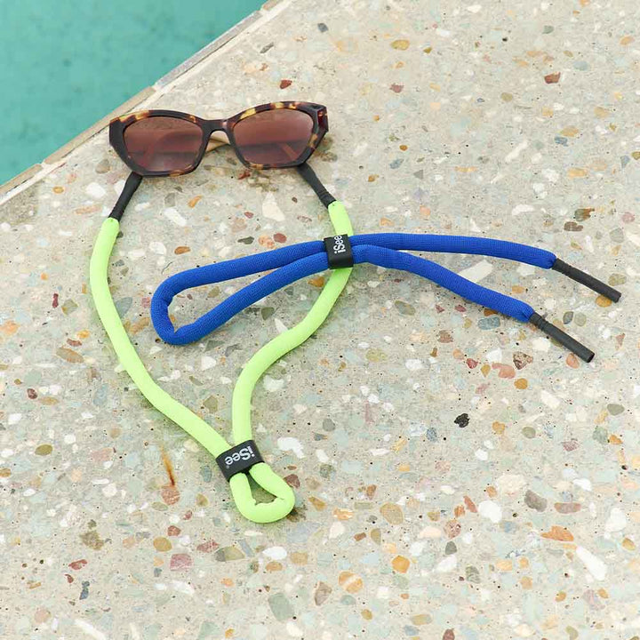 Sunglasses with colorful elastic straps on a textured surface near a pool.