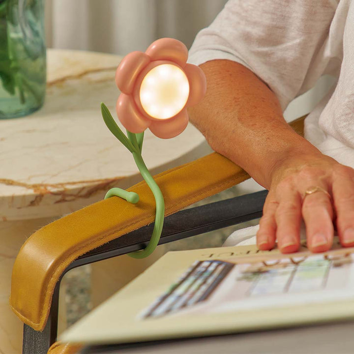 Flower-shaped lamp wrapped on a chair arm with a person reading a magazine