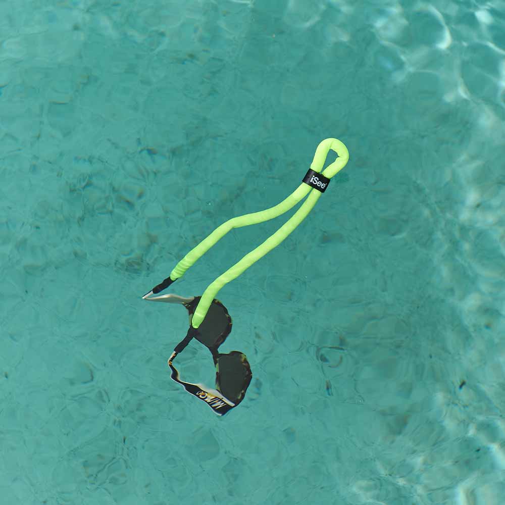 Neon green dog toy with a black tag floating in clear blue water.