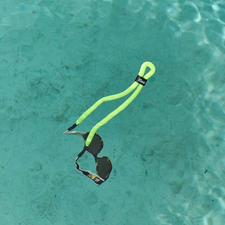 Neon green dog toy with a black tag floating in clear blue water.