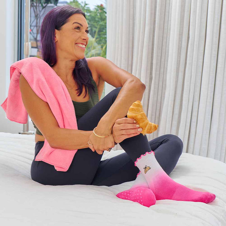 ambre pink and white pilates socks with a frill top on a women sitting a bed