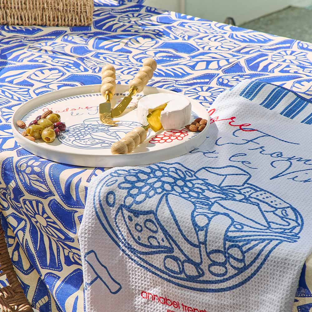 Table setting with a decorative tablecloth, tray with food, and branded towel.