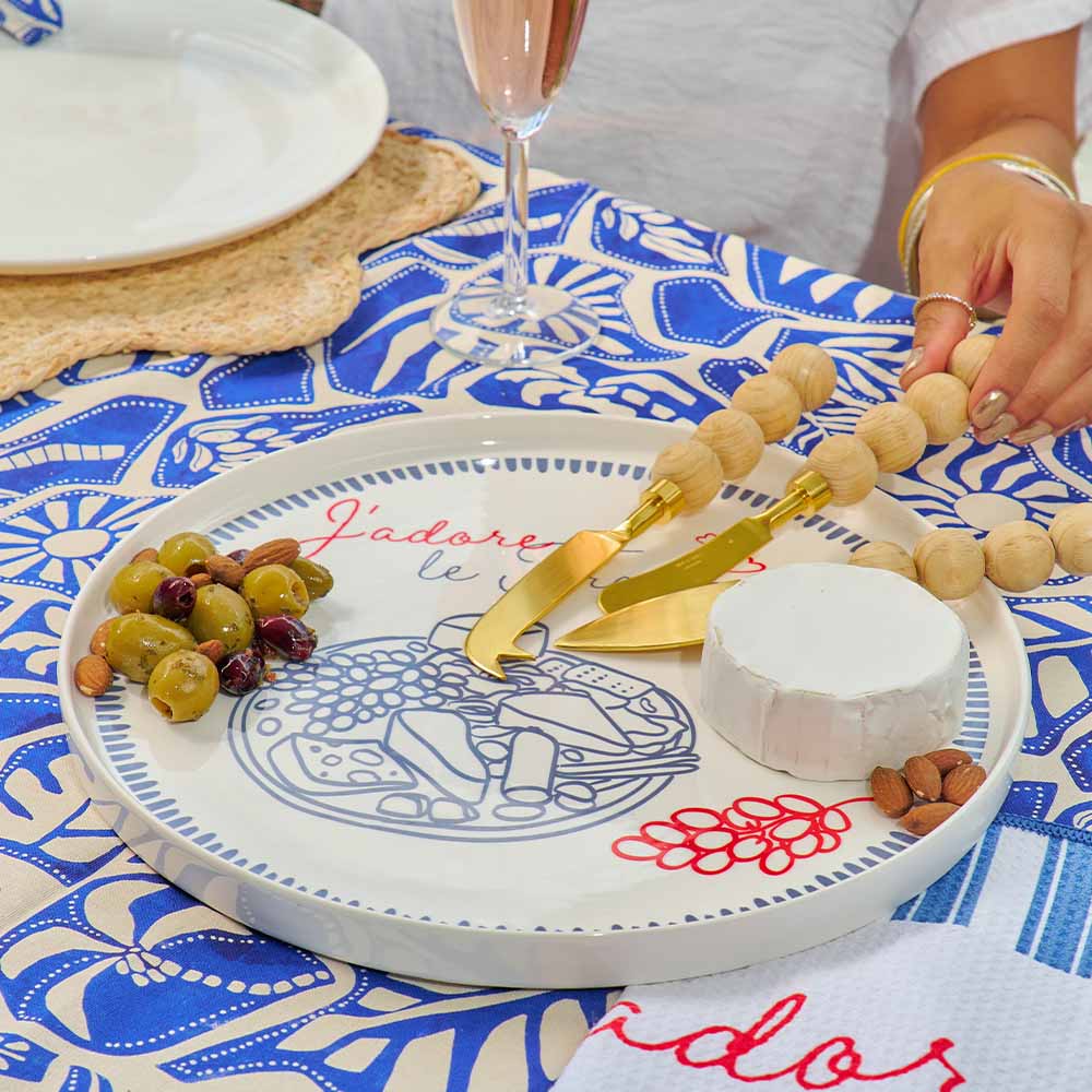 Person preparing a cheese plate with grapes and bread on a decorative plate with 'J'adore' text.