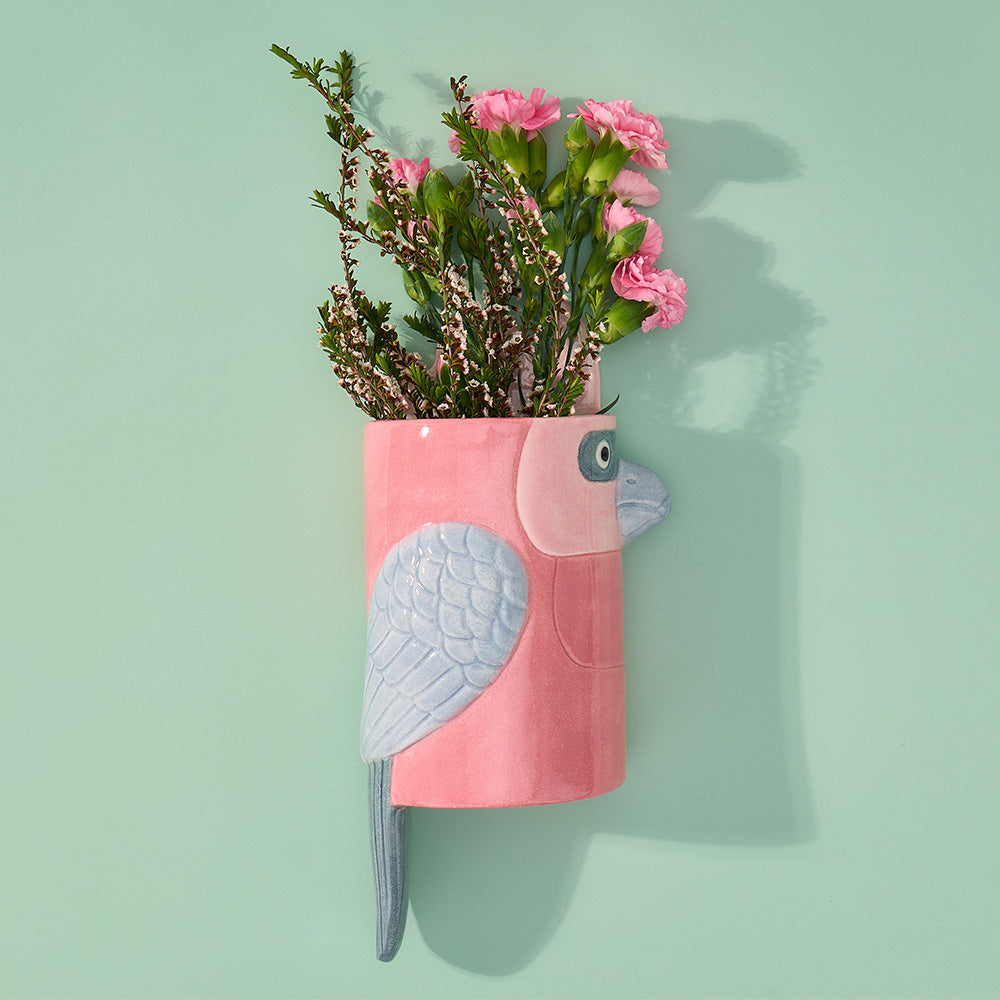 Pink galah-shaped planter with flowers on a light green background