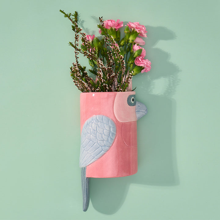 Pink galah-shaped planter with flowers on a light green background