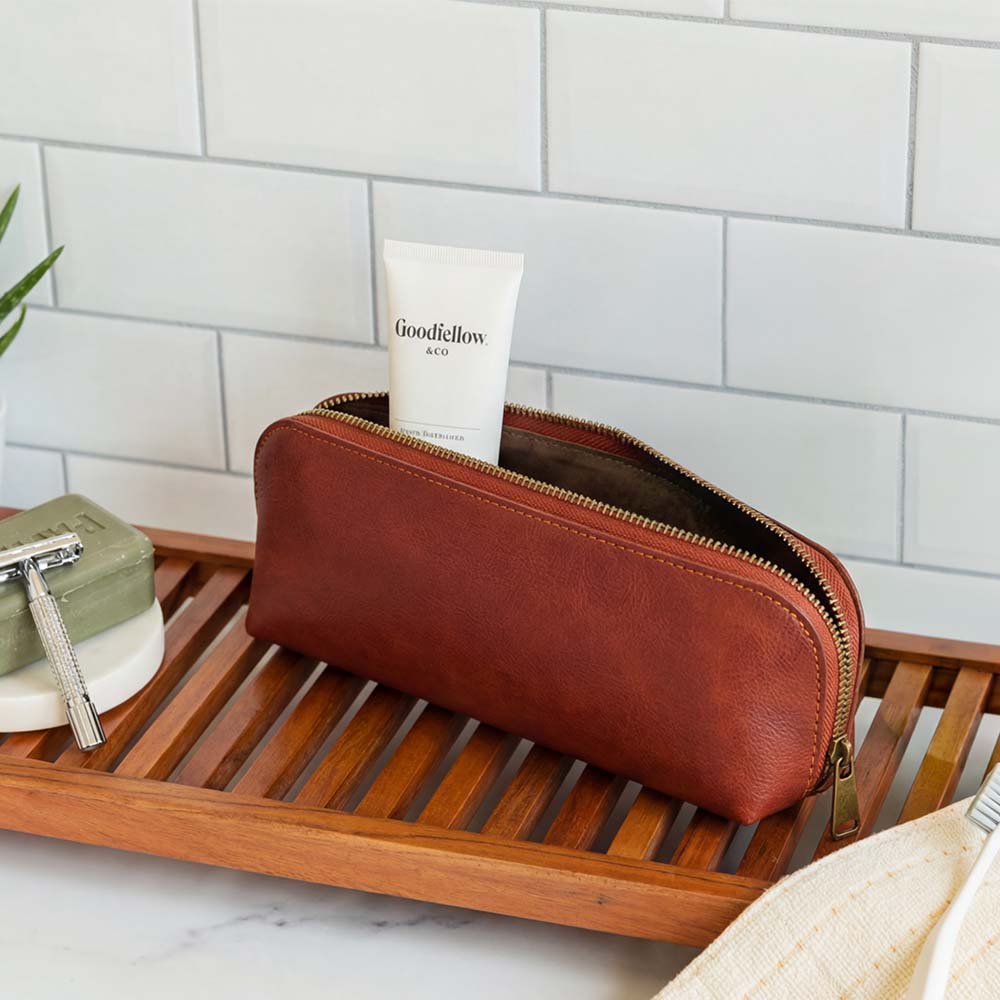 Brown leather toiletry bag with a tube of Goodfellow & Co. cream on a wooden tray.