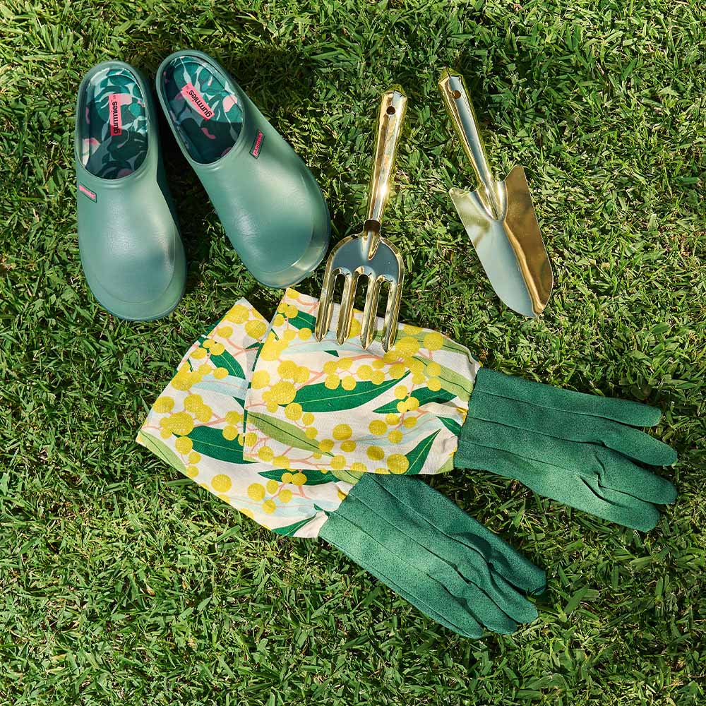 Gardening tools and accessories including green shoes, gloves, and a floral apron on grass.
