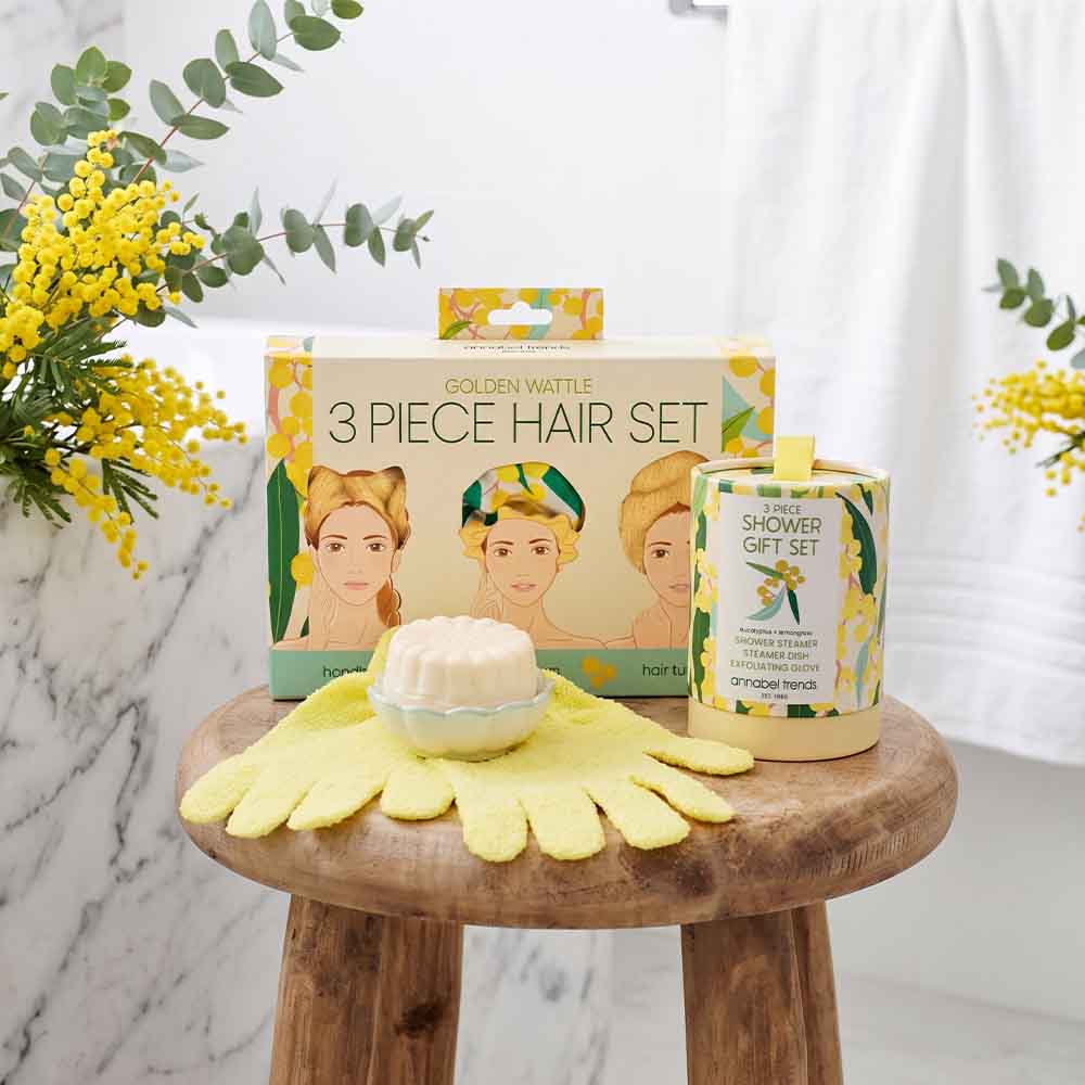 Three-piece hair care set on a wooden stool with yellow flowers and greenery in the background