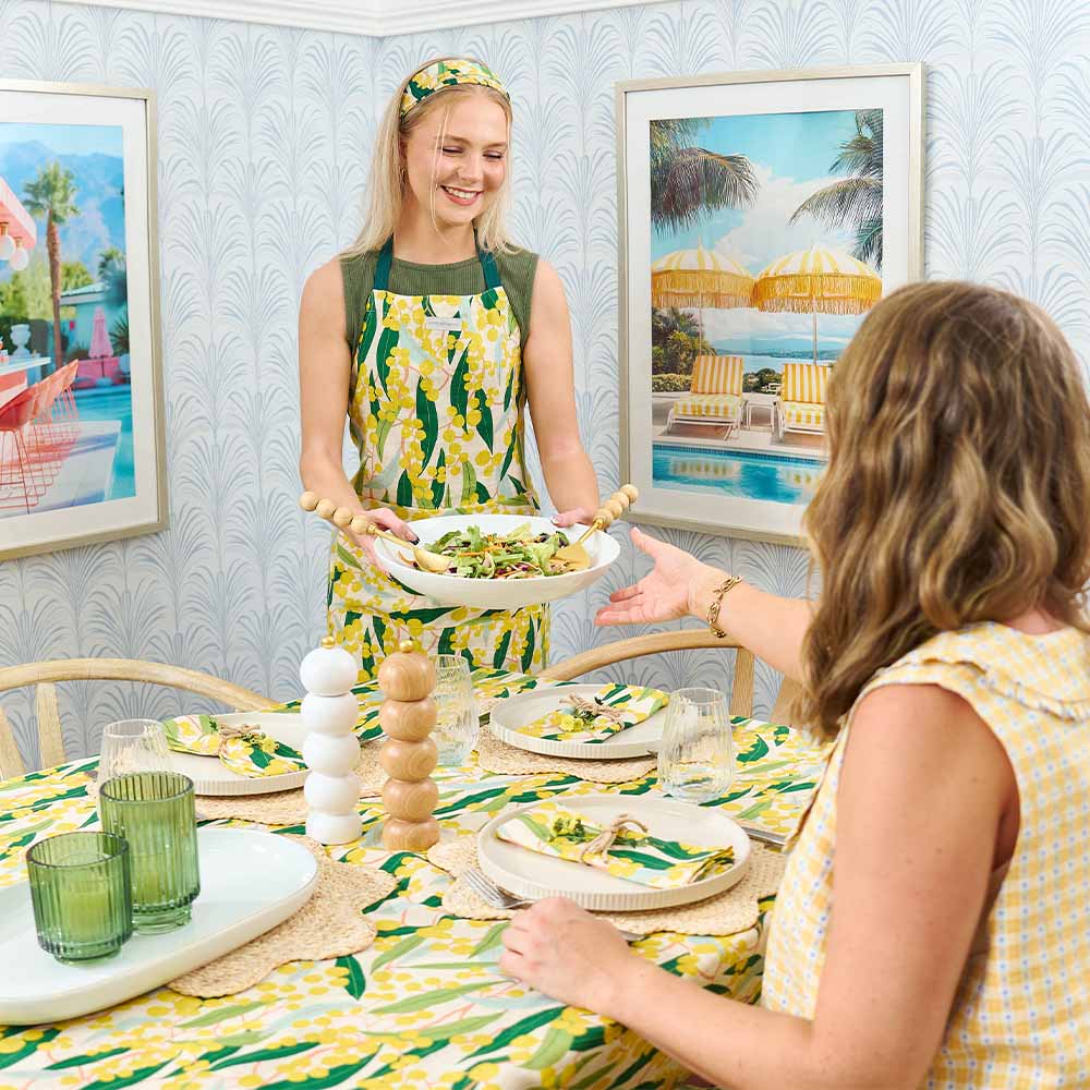 Two women in a dining room with a table set for a meal, surrounded by framed artwork.