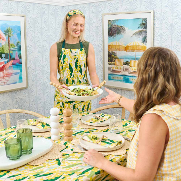 Two women in a dining room with a table set for a meal, surrounded by framed artwork.