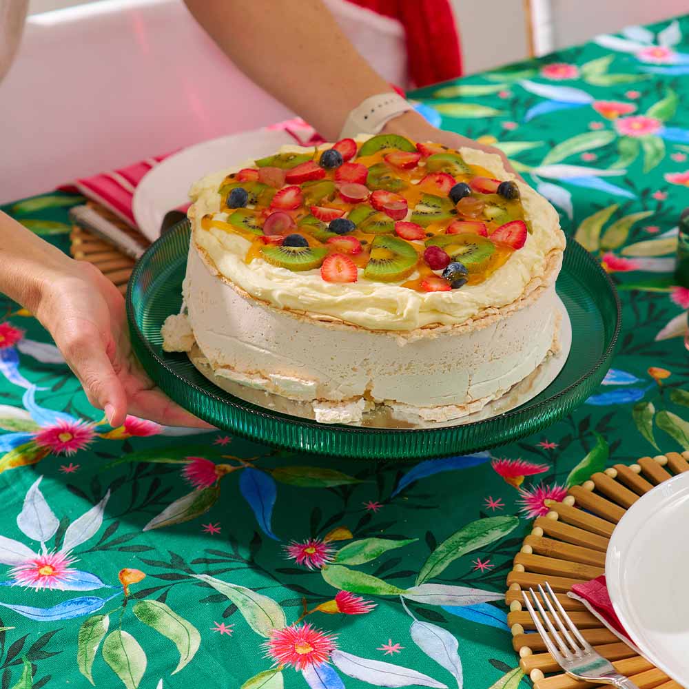 Fruit-topped cake on a green plate with a floral tablecloth