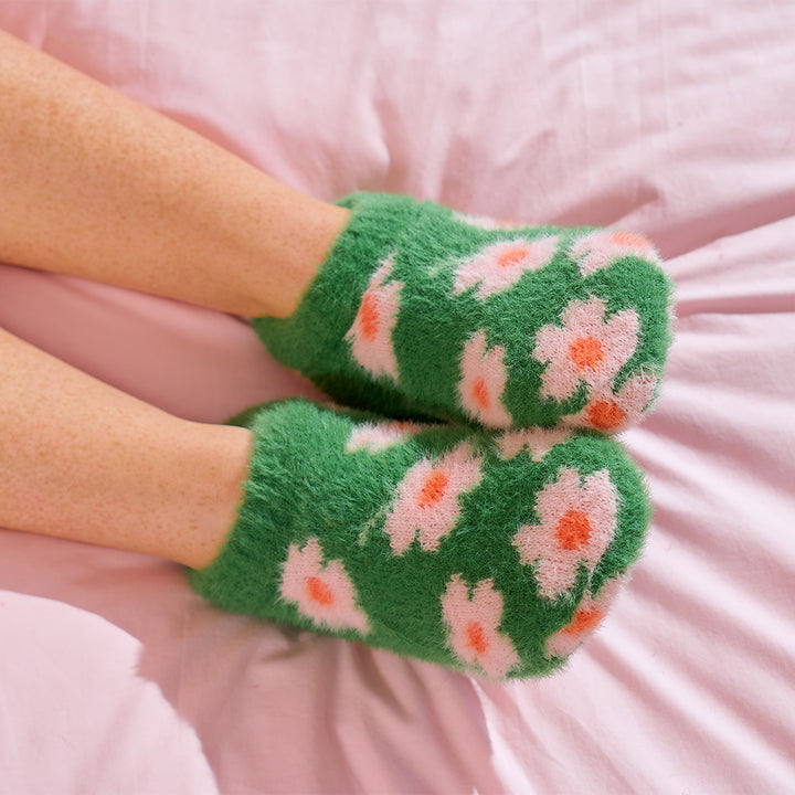 Green socks with floral pattern worn by a person on a pink surface