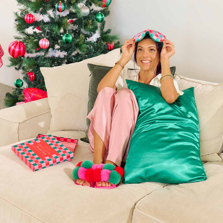 Woman sitting on a couch with festive decorations, including a Christmas tree and gift box.