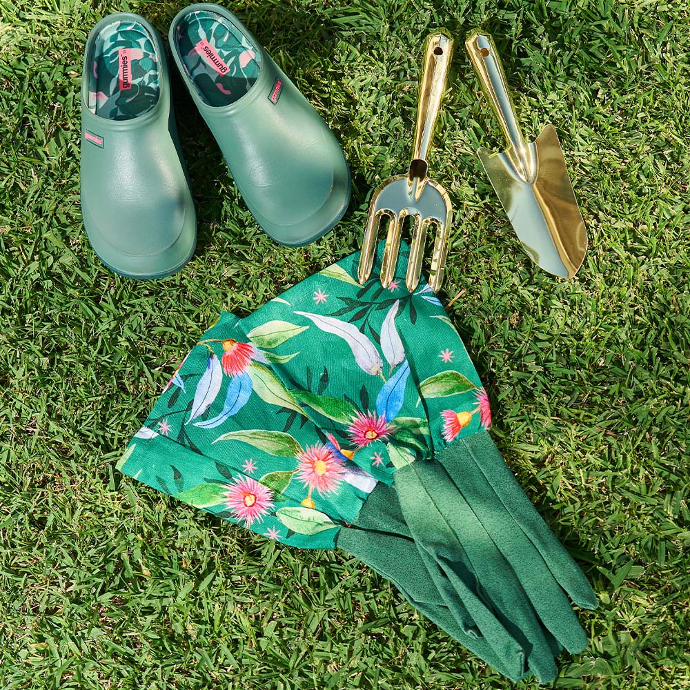 Green gardening shoes, floral apron, and gold tools on grass
