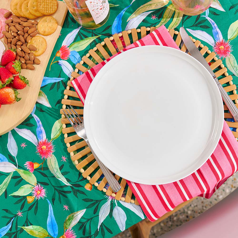 Table setting with a white plate, striped napkin, and fork on a colorful floral tablecloth.