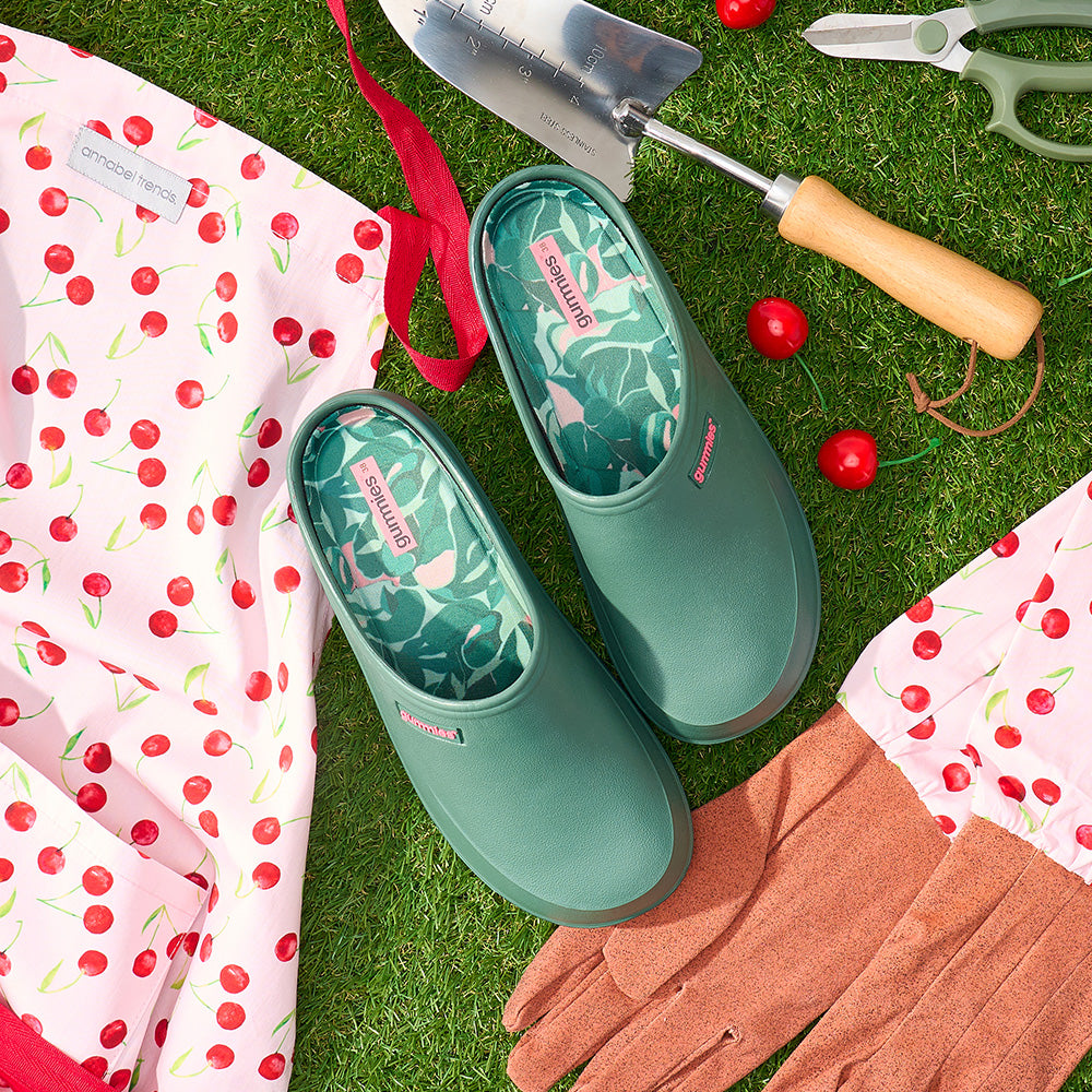 Green garden gummies clogs with floral pattern on grass with gardening tools and fabric.