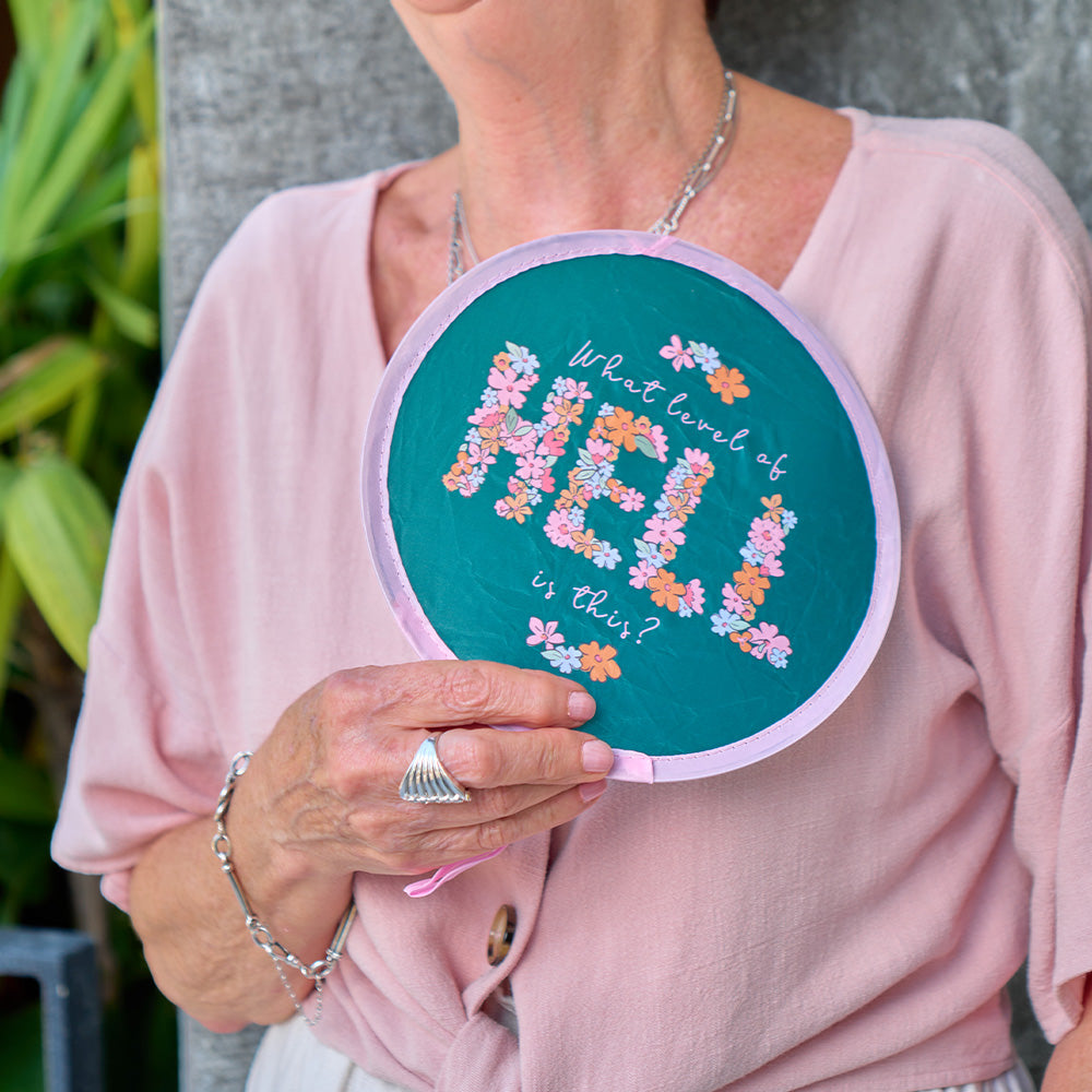 Person holding a circular twist fan with floral text design outdoors
