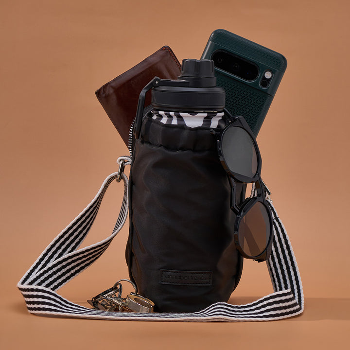 Black water bottle with striped strap, wallet, phone, and sunglasses on a brown background