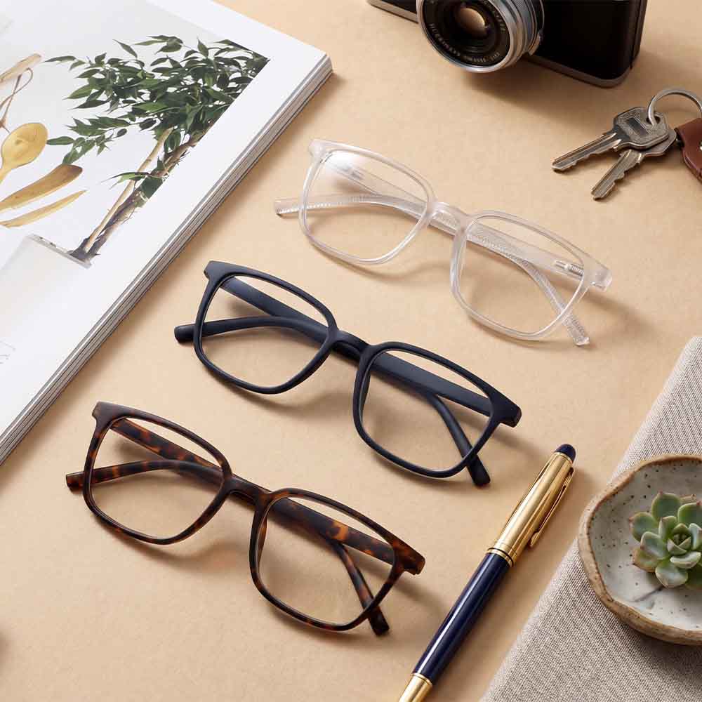 Three pairs of glasses on a desk with a pen and small plant