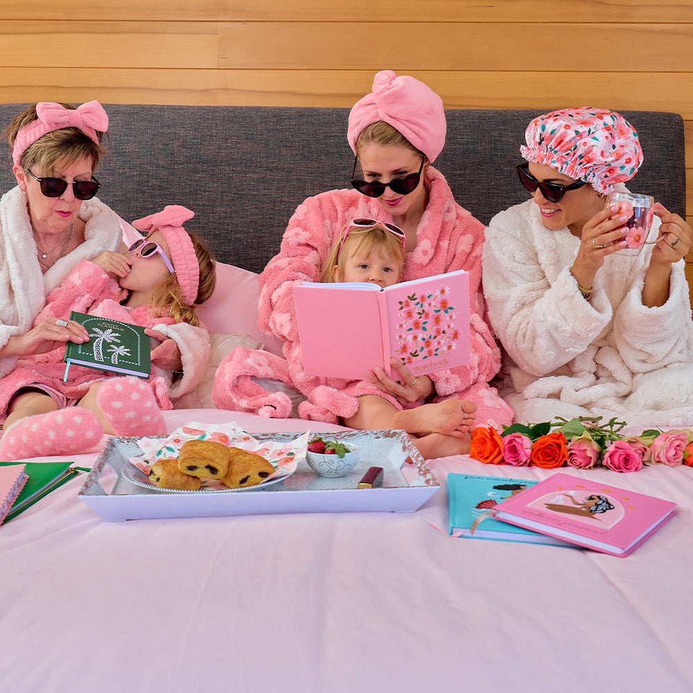 Family of four in bathrobes and hair towels on a bed with snacks and books.