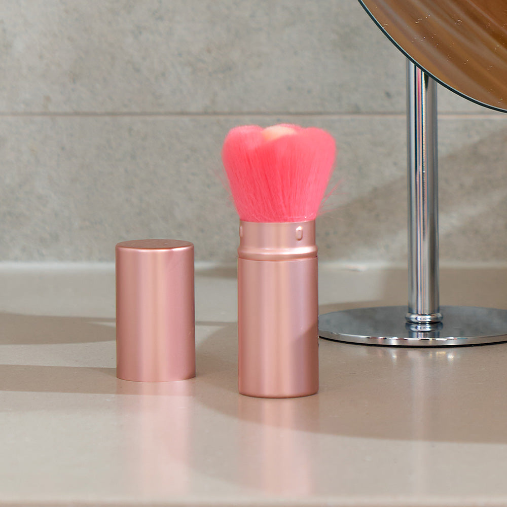 Rose gold makeup brush with pink bristles on a bathroom counter.