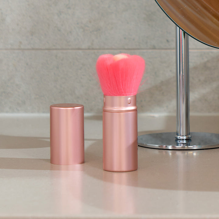 Rose gold makeup brush with pink bristles on a bathroom counter.
