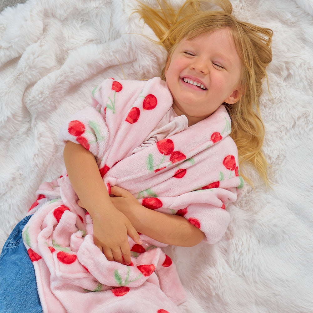 Child wrapped in a pink and red robe with cherries on a white fluffy surface
