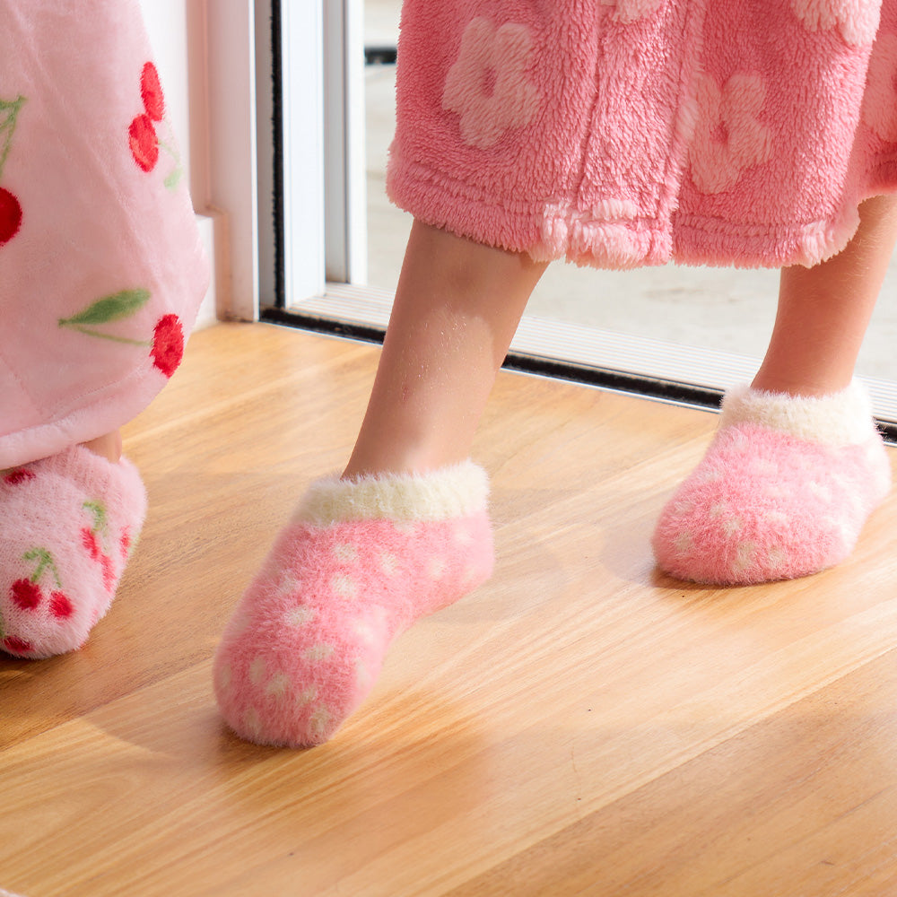 Person wearing pink fuzzy socks and a matching robe on a wooden floor.