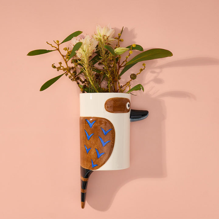 Wall-mounted vase shaped like a kookaburra with flowers on a pink background